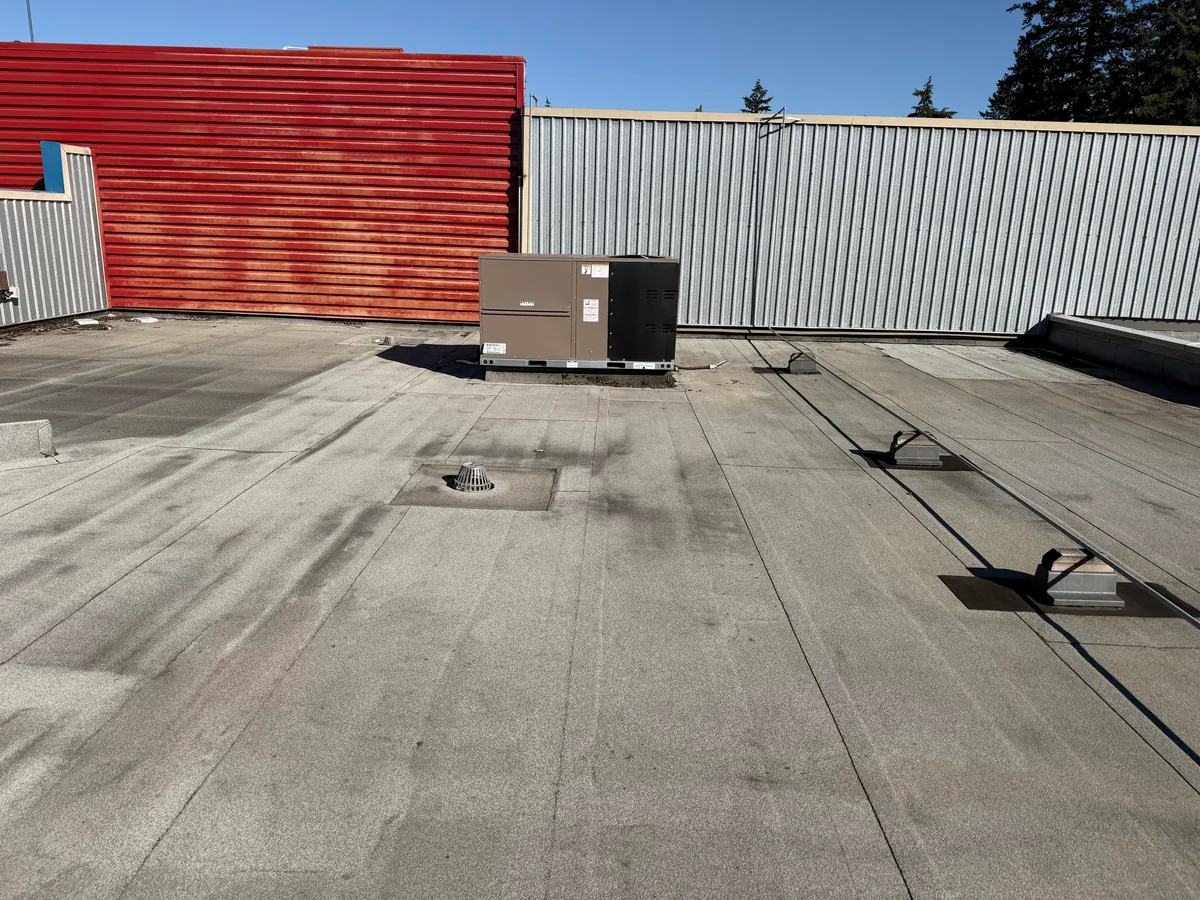 A new package rooftop unit set in place on a flat roof beside a red parapet wall