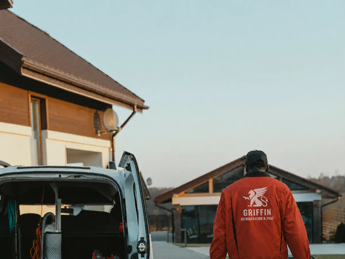 A technician in a Griffin Refrigeration jacket walking from an open service van towards a house